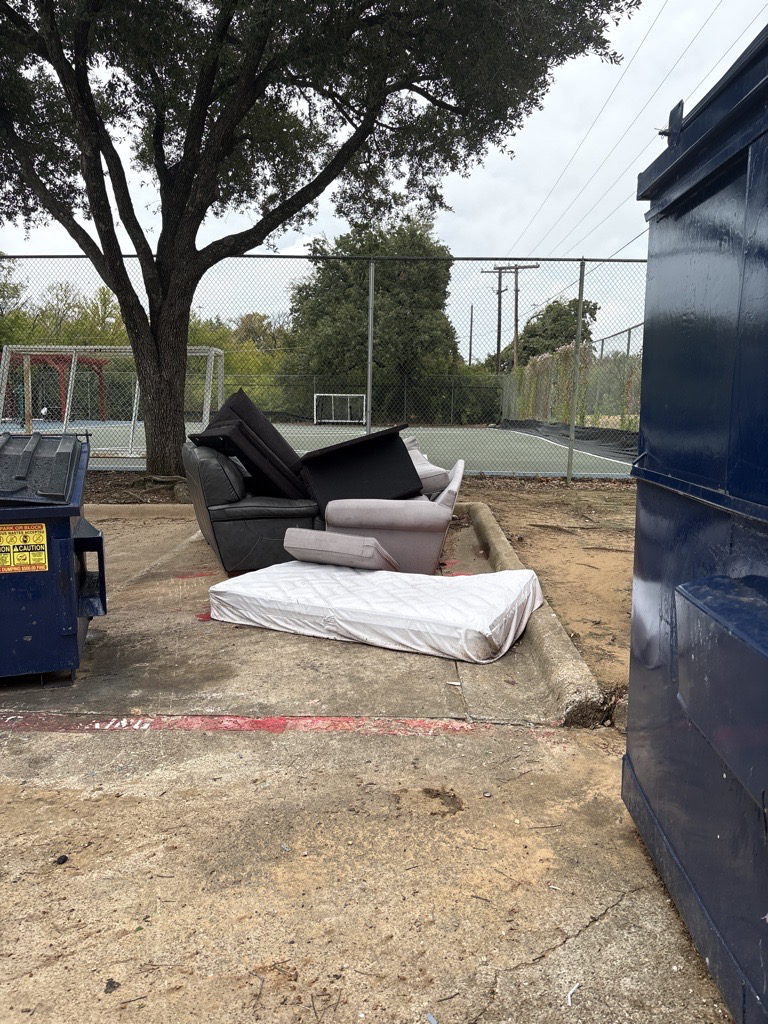 Bulky furniture beside a standard lidded dumpster before pickup